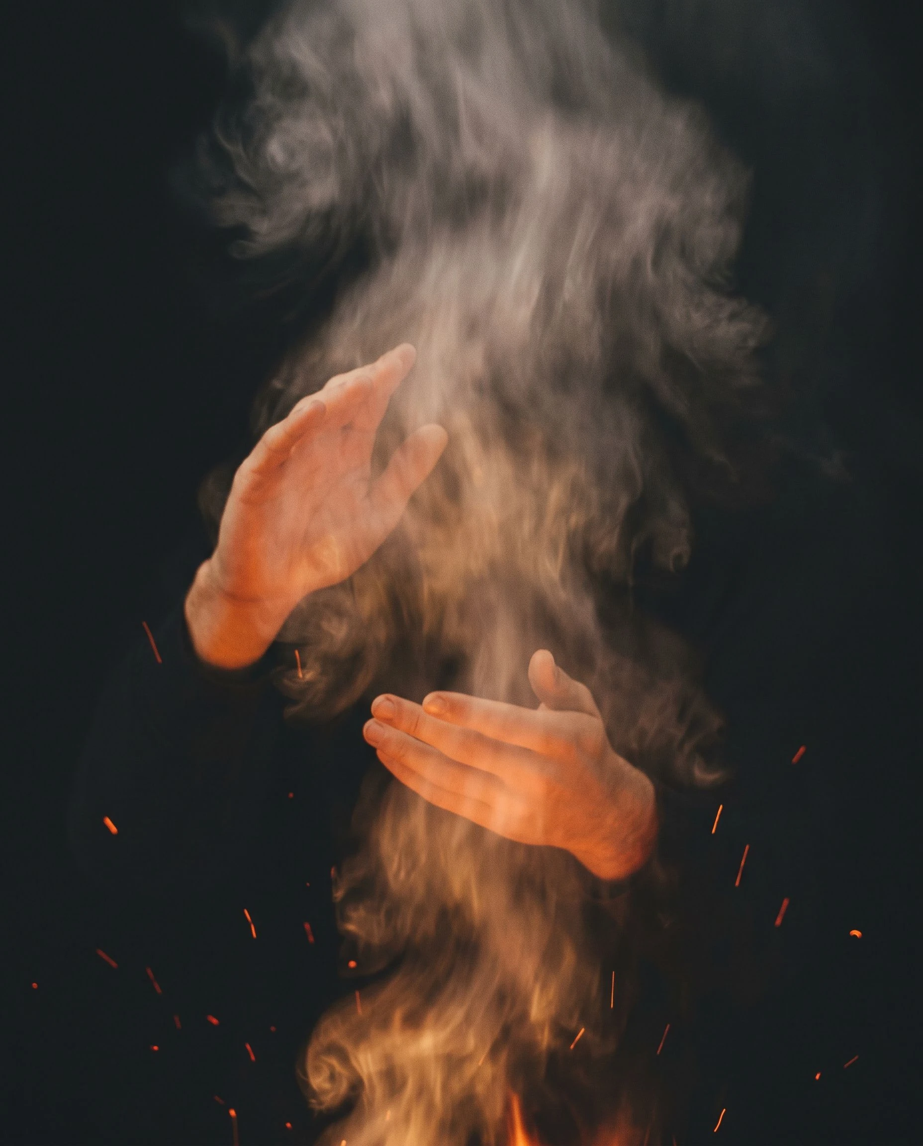 An abstract composition of smoke, firelight, and hands. No face is visible, no dish identifiable. The image is warm and intentionally incomplete.